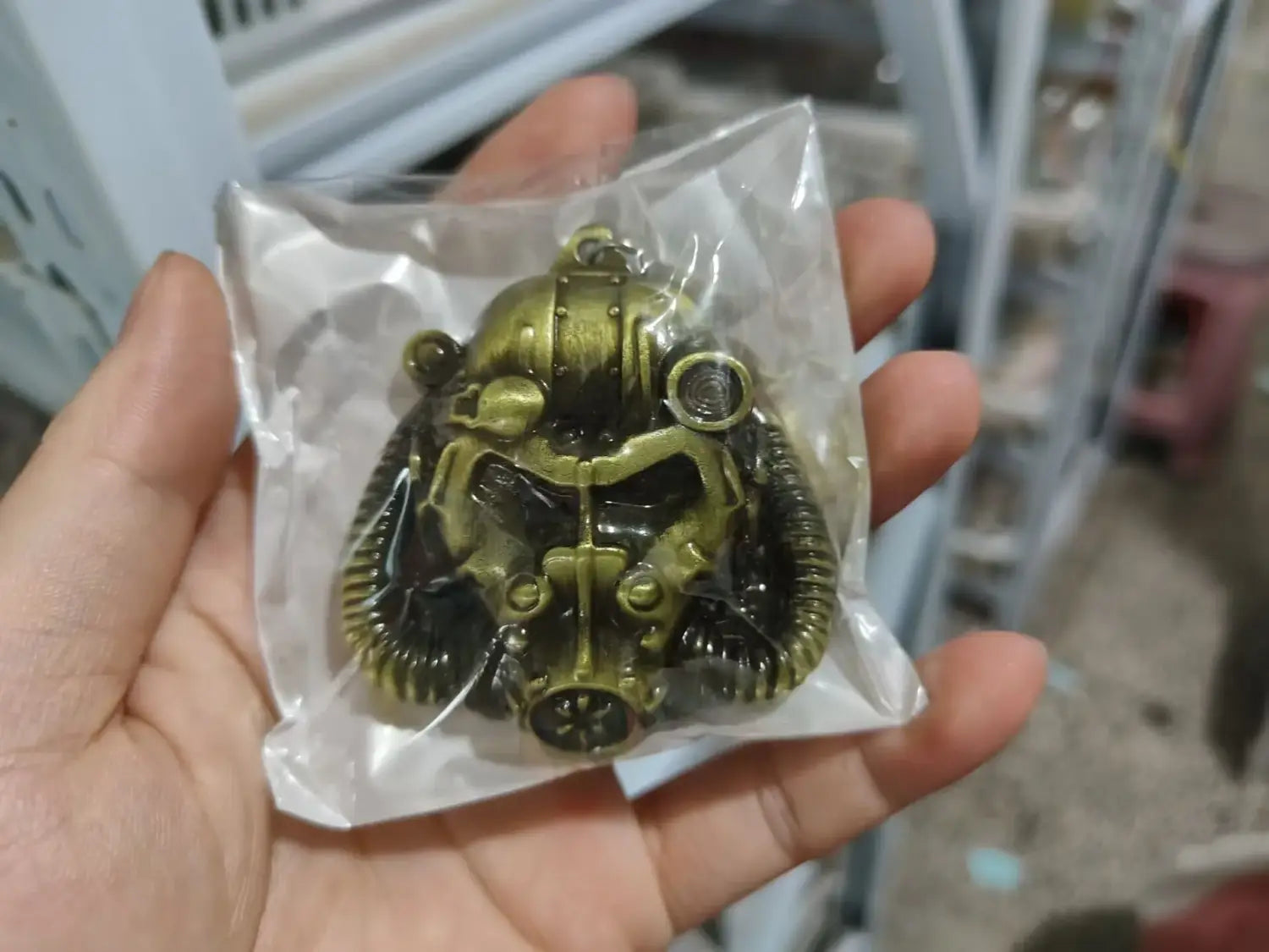 A detailed brass-colored Fallout 76 power armor helmet keychain with black accents and intricate mechanical detailing.