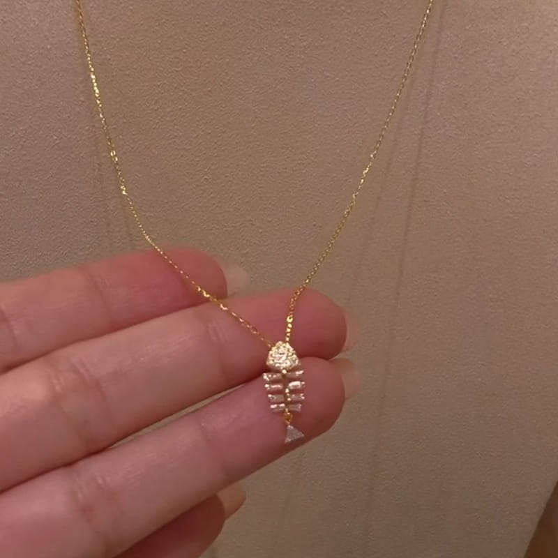 A delicate gold chain necklace featuring a small intricately designed fish skeleton pendant adorned with sparkling clear stones crystal fishbone gold necklace pendant jewelry.