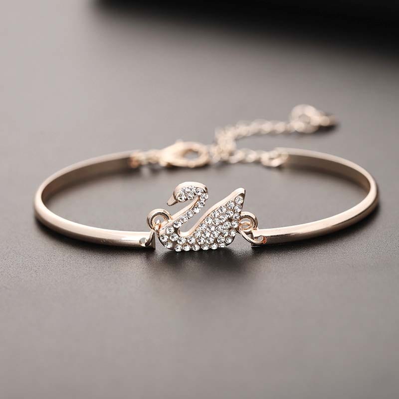 Bracelet jonc délicat à tonalité or rose, présentant une breloque de cygne étincelante ornée de cristaux transparents.