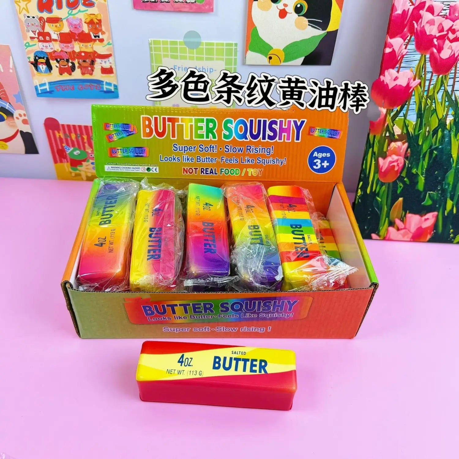 Une barre de jouet antistress souple à la forme de beurre, à rayures arc-en-ciel, dans un emballage rouge et jaune, avec « beurre salé » imprimé dessus, provenant de la collection de jouets antistress souples à la forme de beurre à la fraise à montée lente