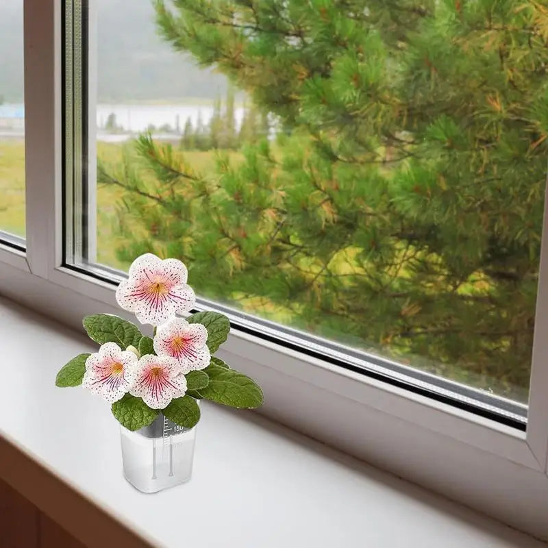 eine zarte weiße Blüte mit rosafarbenen Sprenkeln und gelber Mitte, eingebettet in grüne Blätter, in einem transparenten Pflanzentopf zur Selbstbewässerung, ausgelegt für eine effiziente Bewässerung von Pflanzen