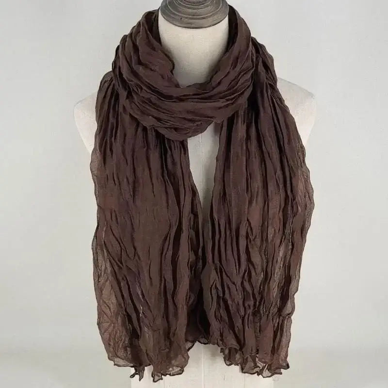 Una bufanda de algodón lino color marrón chocolate suave para mujer, con tela transpirable y ligera drapeada con elegancia alrededor del cuello de un maniquí.