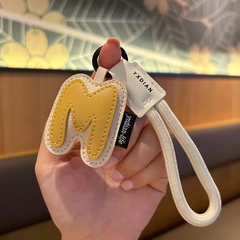 Leather initial keychain letter wristband charm in yellow and cream-colored leather featuring a stitched letter m design.