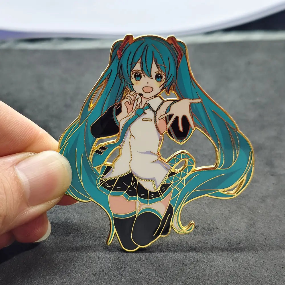 a shiny gold-trimmed enamel pin metal badge featuring the anime character hatsune miku with vibrant teal hair wearing a white blouse and black skirt.