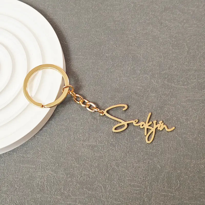 Gold-colored metal customized name keychain set featuring the name seokjin in elegant cursive script.