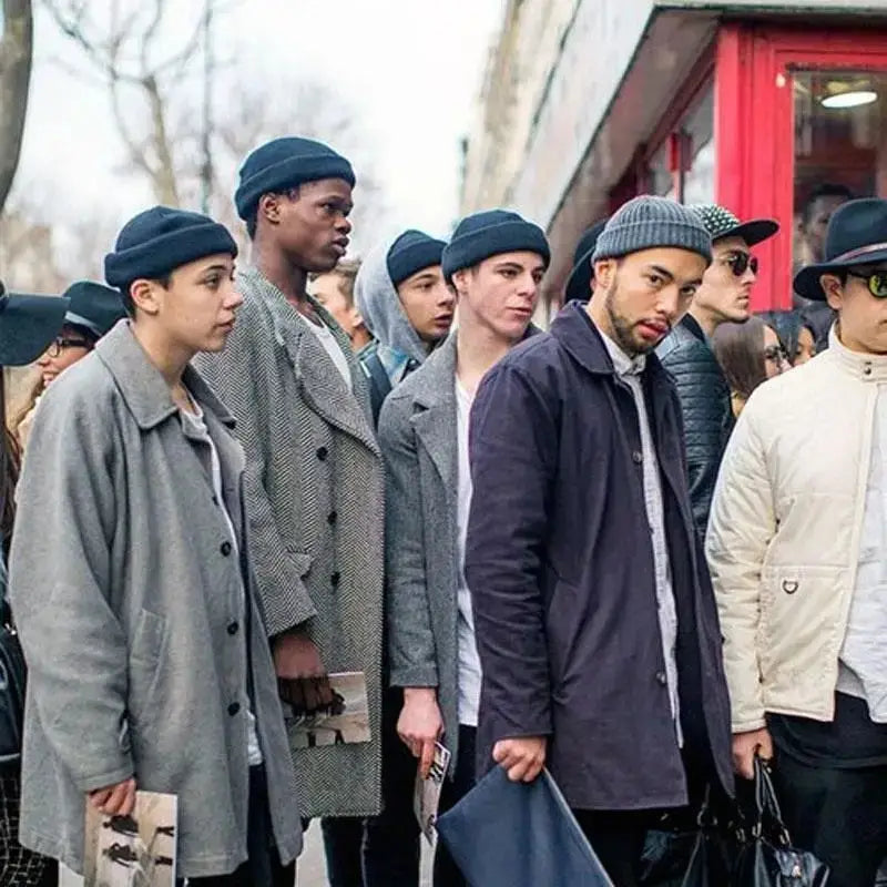 A group of men wearing dark blue and gray ribbed knit winter beanie hats with layered coats in an urban streetwear style.