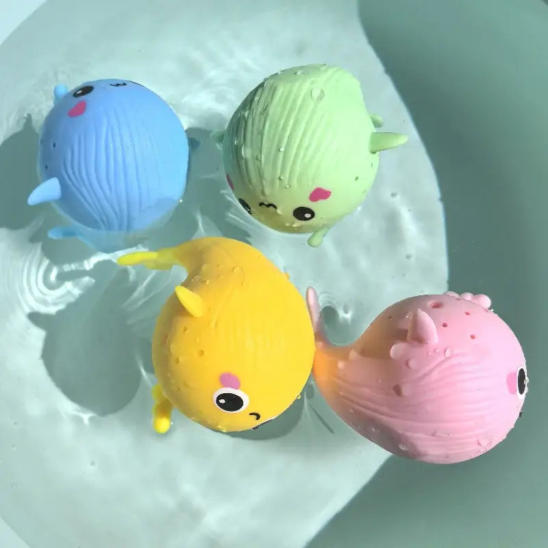 Vier bunte Plüsch-Blauwal-Badeschwamm-Wasser-Spielzeuge für Kinder mit niedlichen Gesichtsausdrücken und strukturierten Körpern, die im Wasser treiben.