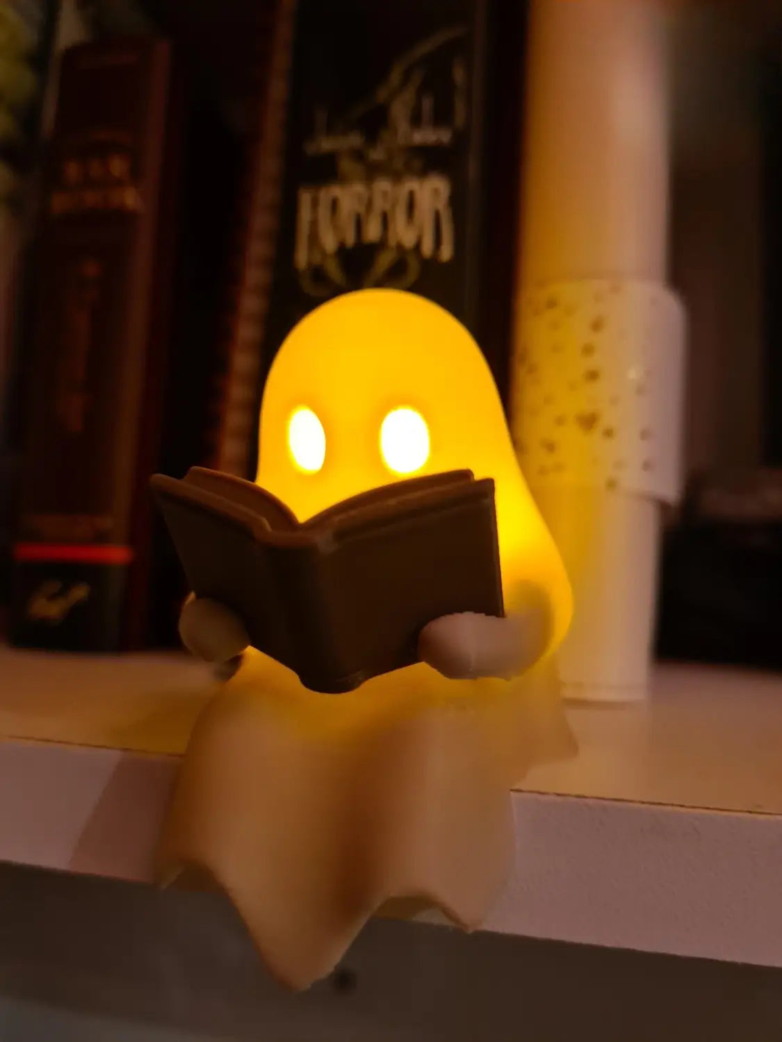 Eine leuchtend gelbe Geister-Lese-Buchfigur, die ein Buch mit leuchtenden Augen hält, mit einem flackernden Teelicht.