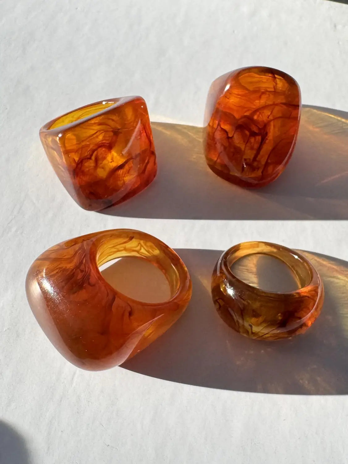 Set of four amber-colored translucent chunky resin cocktail rings with swirling marbled patterns.