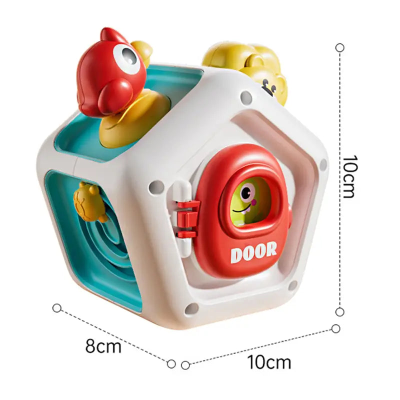 Jouet de voyage cube d’occupation Montessori en plastique blanc et turquoise, avec une porte rouge, des figurines de canard jaune et un visage souriant sur la face avant.