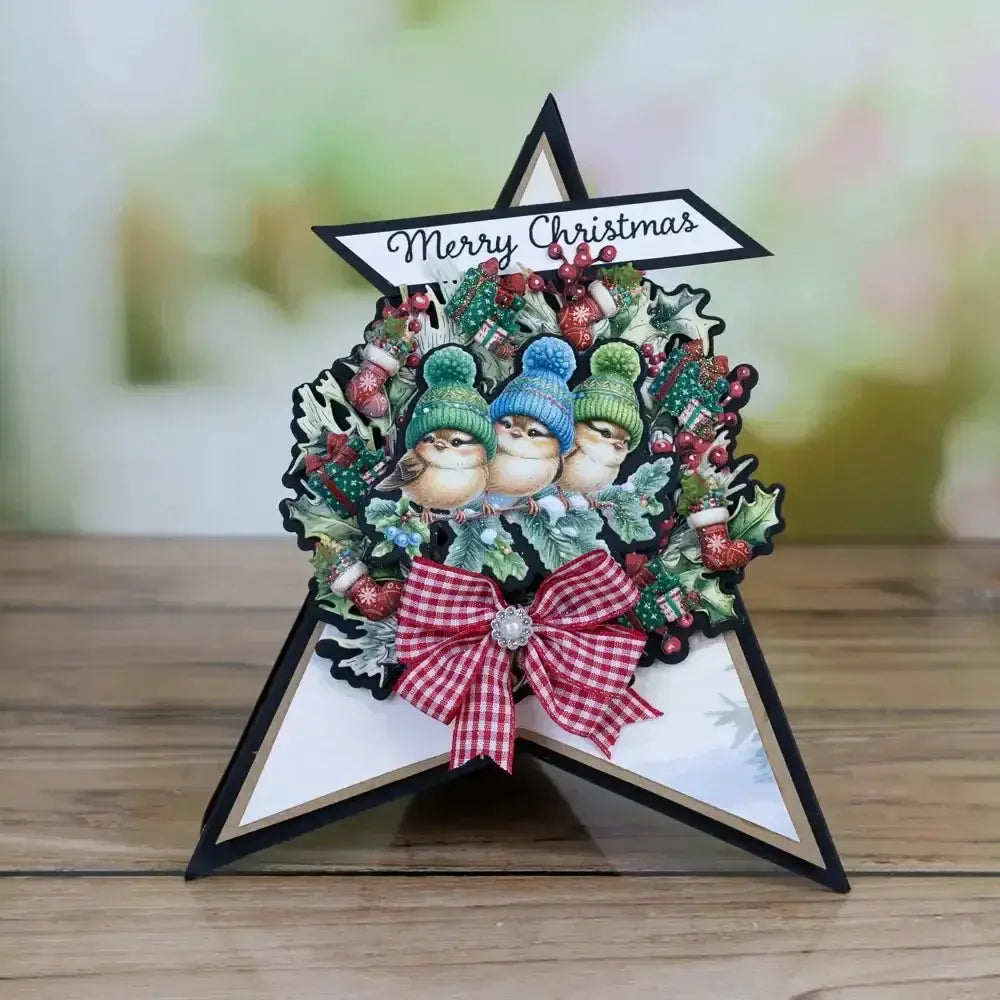 a christmas metal cutting die and stamp set featuring a festive card design with three birds in colorful knit hats nestled in a holly wreath decorated with berries ornaments and a red and white checkered bow at the center