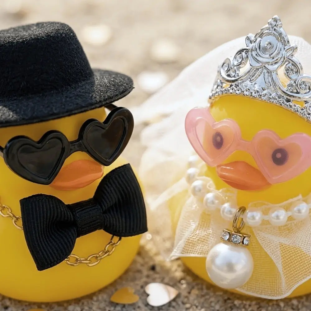 patito de goma amarillo que lleva una diadema plateada, gafas rosadas con forma de corazón y un collar de perlas con un colgante; se presenta en un conjunto de adorno de pareja de patitos de goma para boda