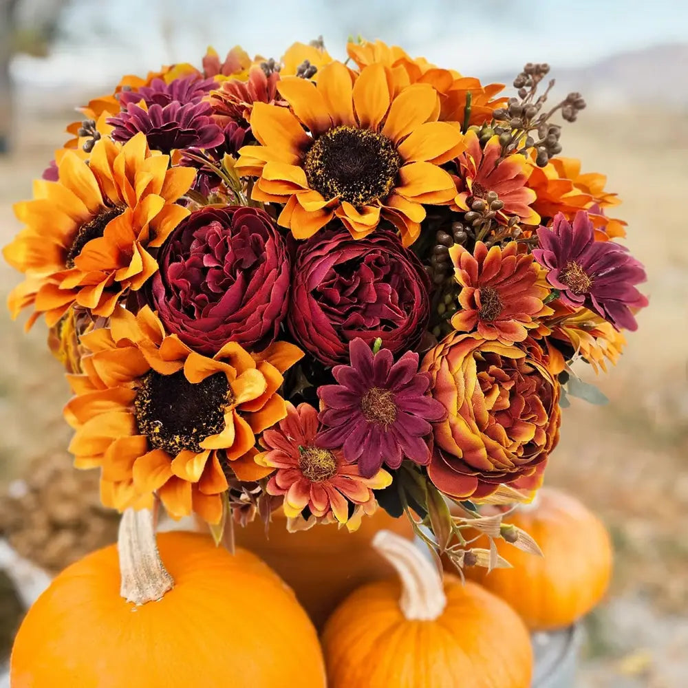 a vibrant artificial flowers autumn sunflower bouquet with orange and deep maroon flowers arranged with decorative pumpkins for home decoration and to send flowers.