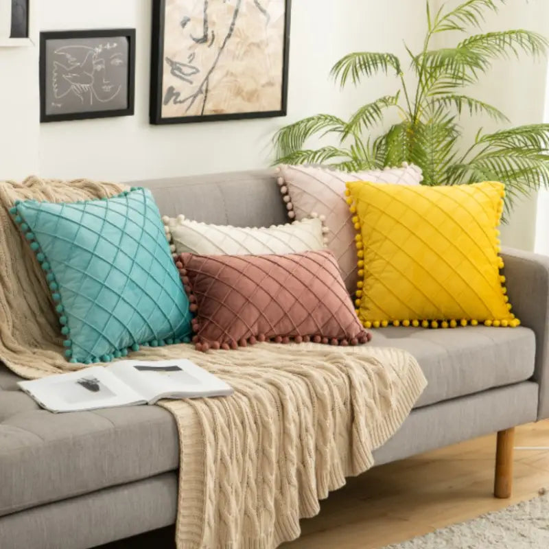 canapé en velours gris confortable, décoré de housses de coussin matelassées colorées avec garniture à pompons, recevant des retours positifs.