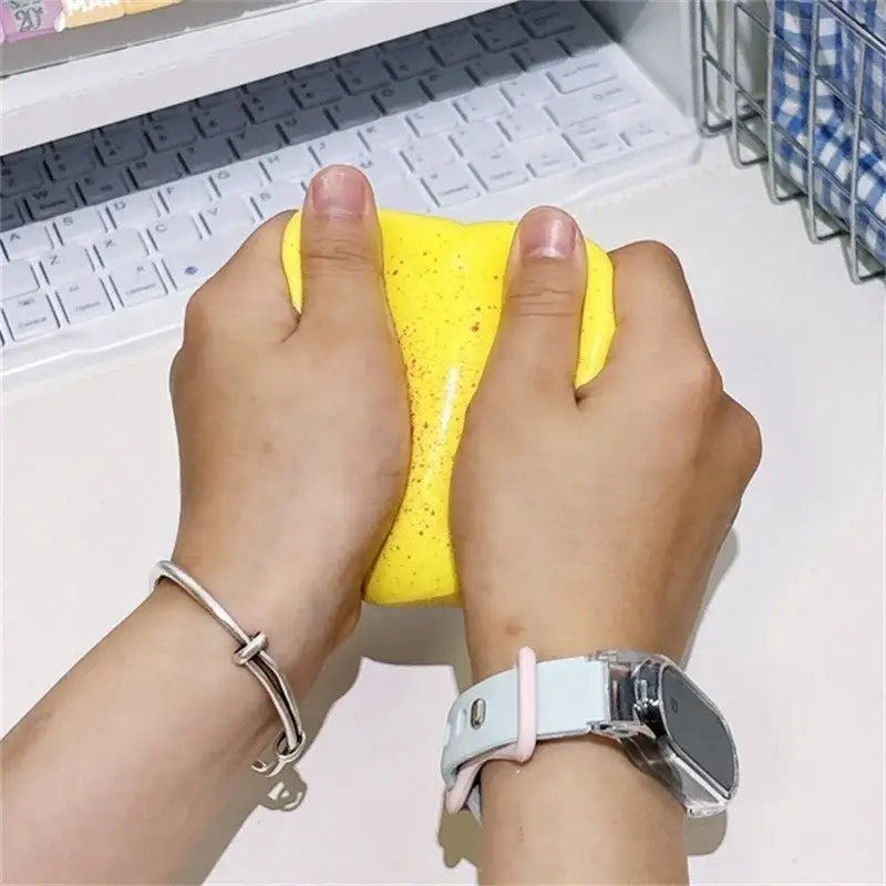 De la pâte à slime jaune tachetée est pressée entre deux mains, dans le cadre du jouet anti-stress en forme de toast moelleux, couleur macaron.