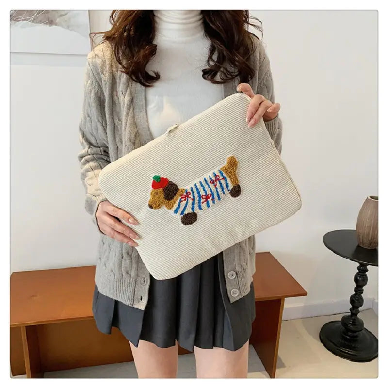Beige Kord-Laptophülle für MacBook Pro als Beutel mit einem strukturierten Clutch-Design, bestickter Dackel in blau-braunen Streifen, rote Mütze