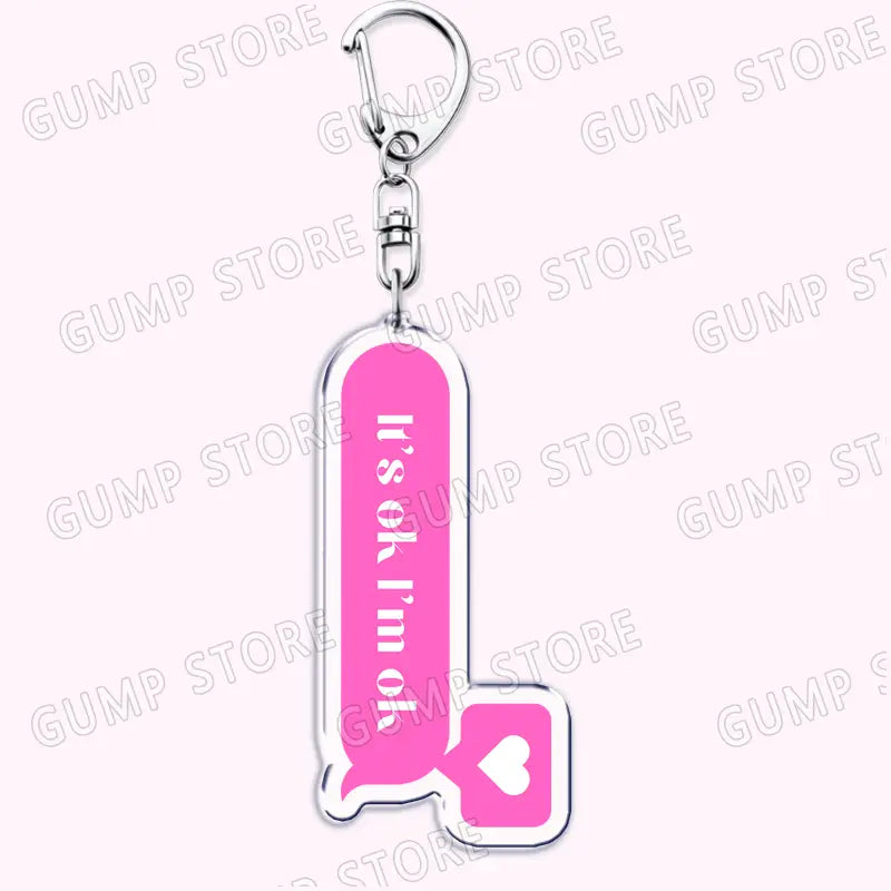 Pink acrylic Tate Mcrae keychain shaped like a speech bubble with the text its ok im ok and a heart symbol, designed as a music fan gift.