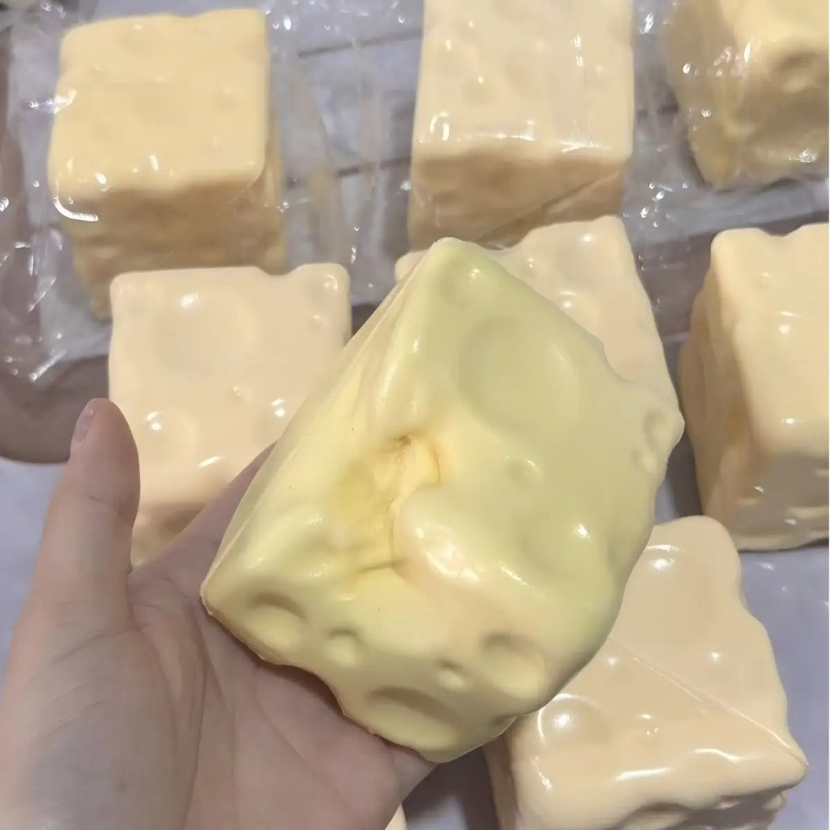 ein blassgelber Käsewürfel-Stressball, ein knetbarer Sinnes-Plaything, geformt wie ein quadratischer Seifenriegel mit einer strukturierten Oberfläche, die Schweizer-Käse-Löcher nachahmt