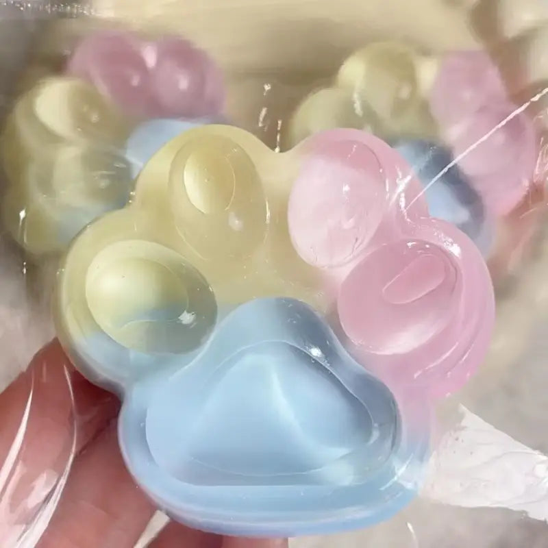 Jouet anti-stress souple et moelleux en silicone translucide pastel, en forme de patte d’arc-en-ciel, fabriqué en matériau souple et translucide en silicone.