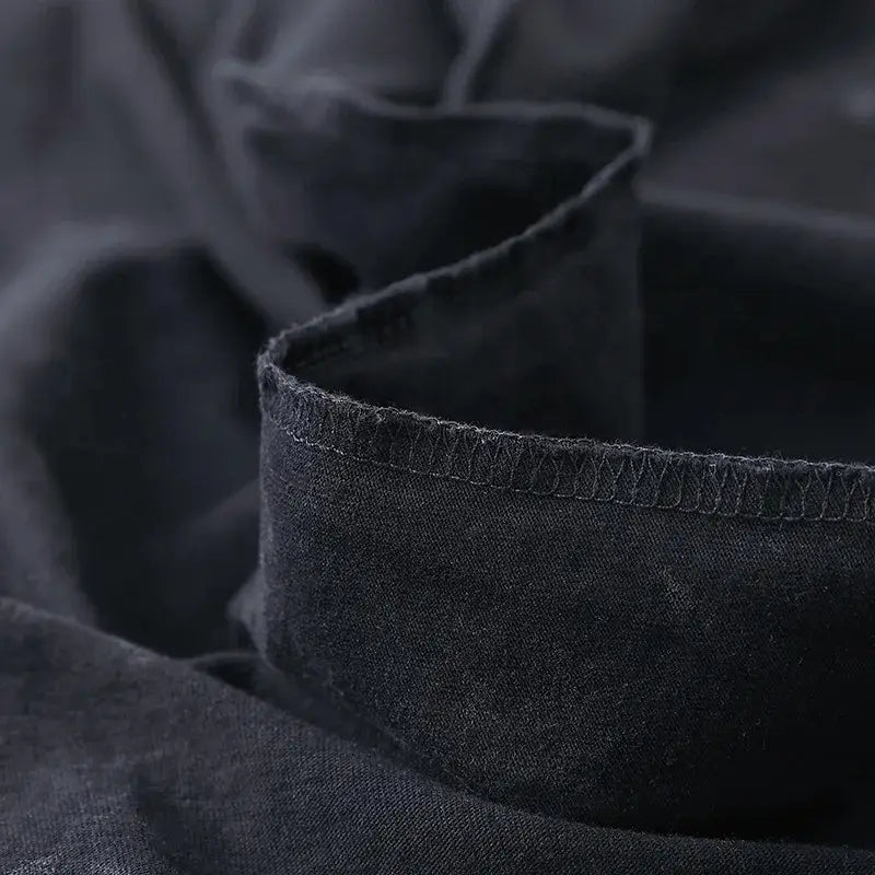 Tela de mezclilla (denim) gris oscuro con una textura ligeramente desgastada y costuras visibles a lo largo del borde doblado, en una camiseta extragrande vintage lavada y desteñida con gráfico de anime gótico.