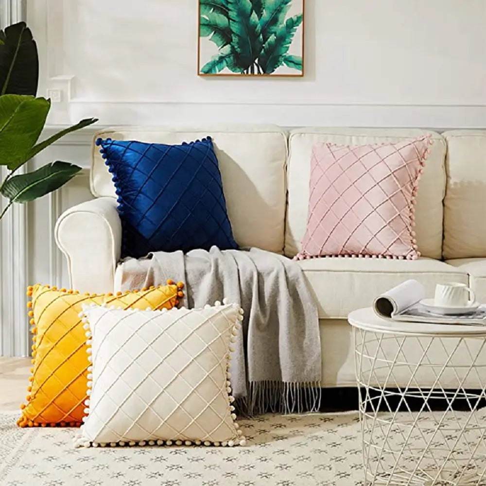 ensemble de quatre housses de coussin carrées en velours gris avec garniture duveteuse à pompons, dans des bleus vifs, rose doux, jaune ensoleillé et blanc crème, présentant un motif matelassé en losange recevant des retours positifs.