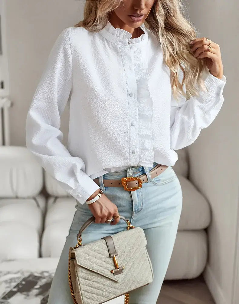 Un bolso acolchado color beige con herrajes de tono dorado y correa de cadena, combinado con una blusa blanca de textura con manga larga y volantes.