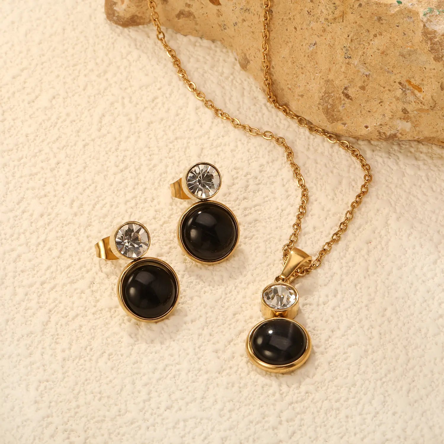 Gold-toned stainless steel necklace and earring set featuring black oval opal stones and clear crystal accents