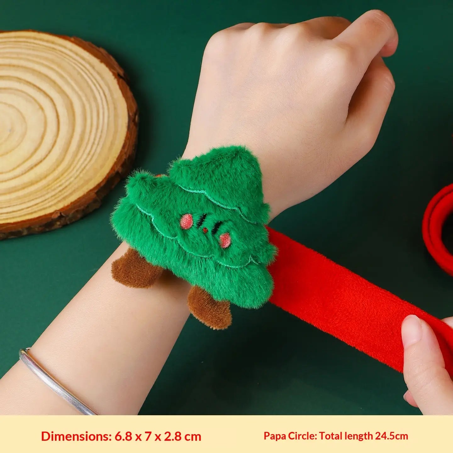 Pulsera tipo eslogan navideña esponjosa verde para niños, con un brazalete suave con forma de árbol, pies marrones y ojos rosados bordados, sujeta a una tira elástica roja.