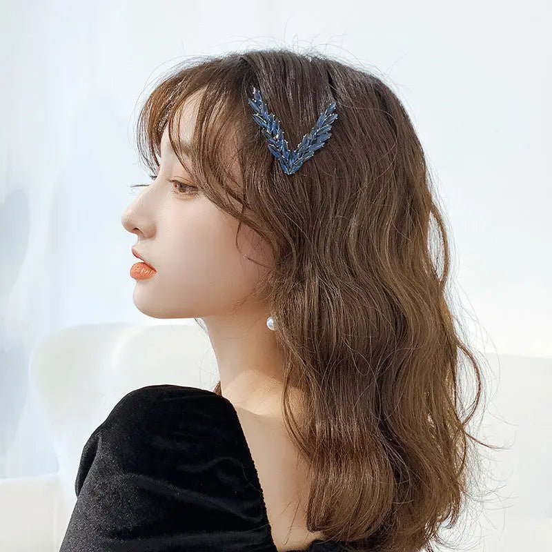 A delicate blue feather-shaped crystal v shape hair clip with a sparkling textured surface.