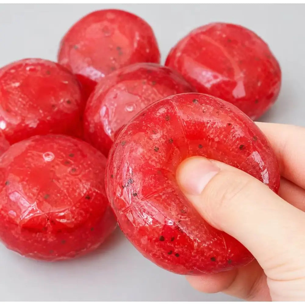 un juguete translúcido de gel rojo, de rebote lento, para aliviar el estrés, con motitas negras que se asemejan a una bolita artesanal de granizado de sandía