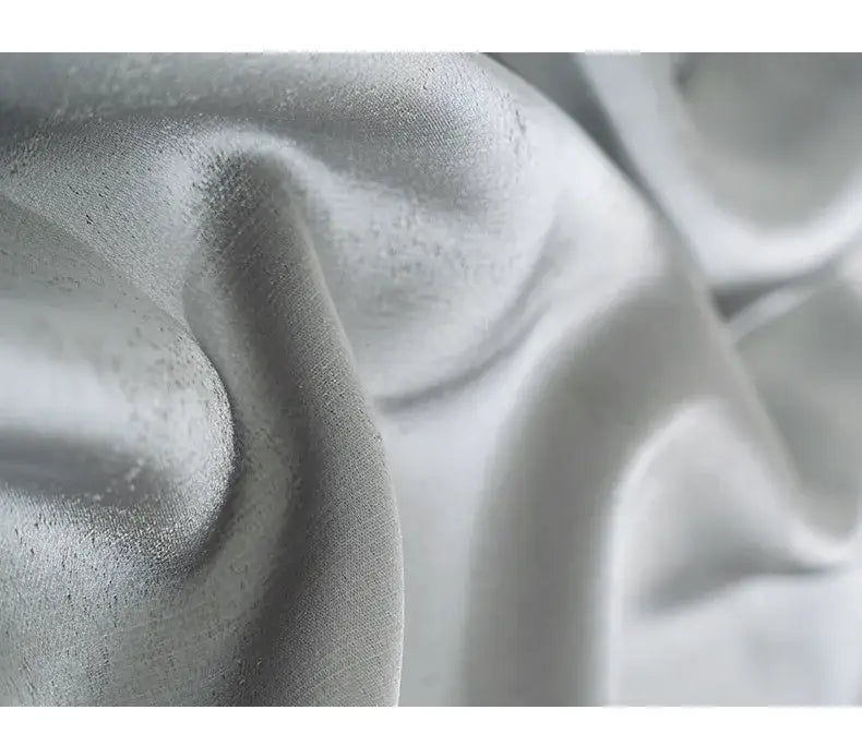 A soft silvery-gray satin fabric with a smooth reflective surface and gentle folds used in living room curtains custom blackout drapes para la sala.