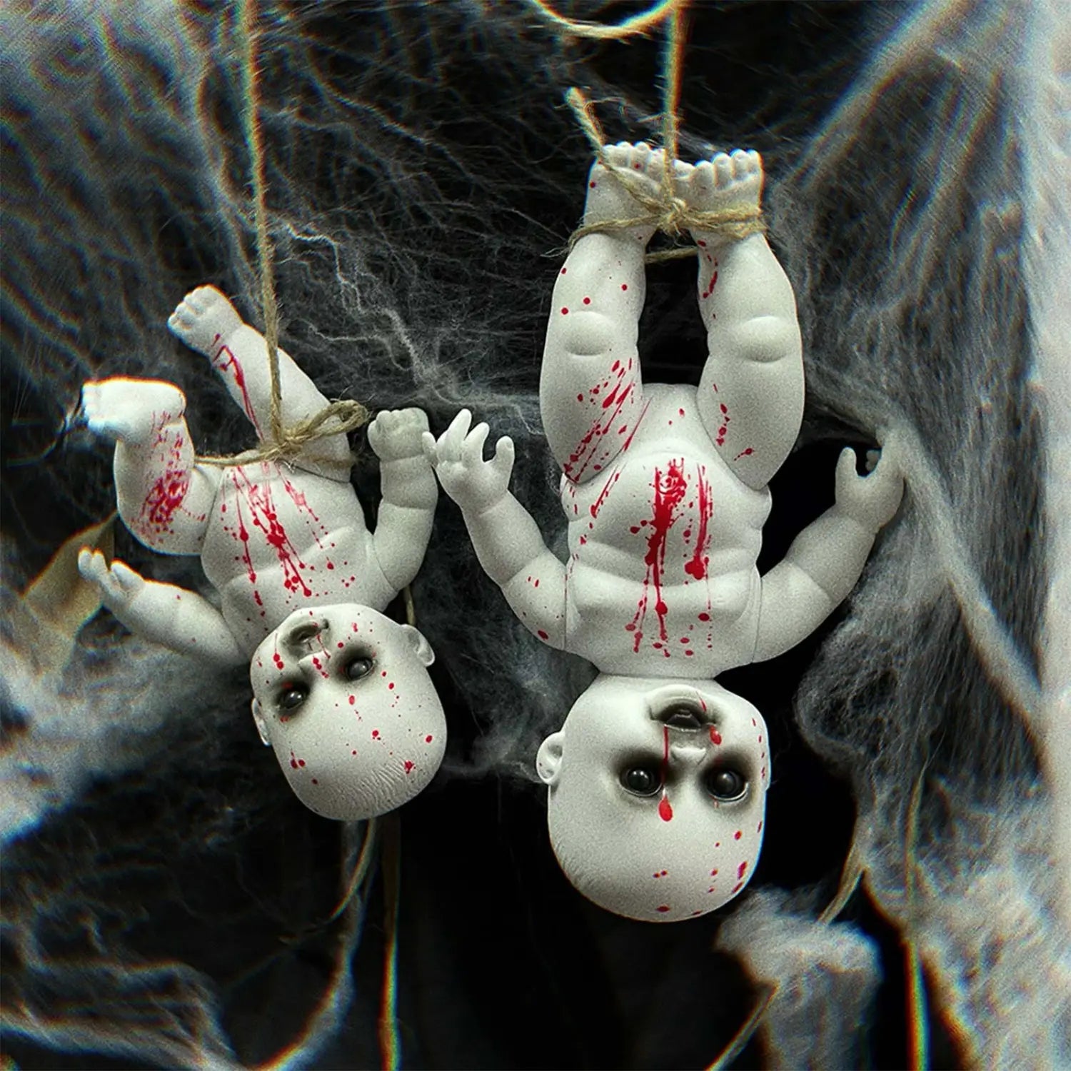 two white plastic baby dolls with red splatter paint hanging upside down by twine as a halloween hanging ghost doll spooky prop.
