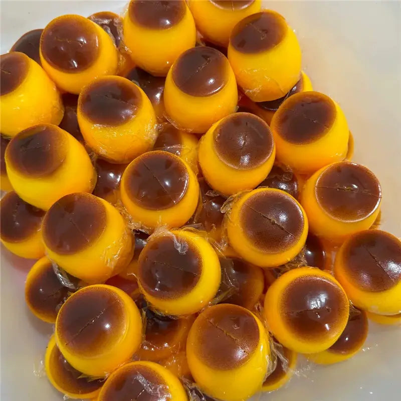 Jouet sensoriel de type balle anti-stress en forme d’arachide présentant des bonbons gélifiés en couches jaune et brun, enveloppés dans un plastique transparent.