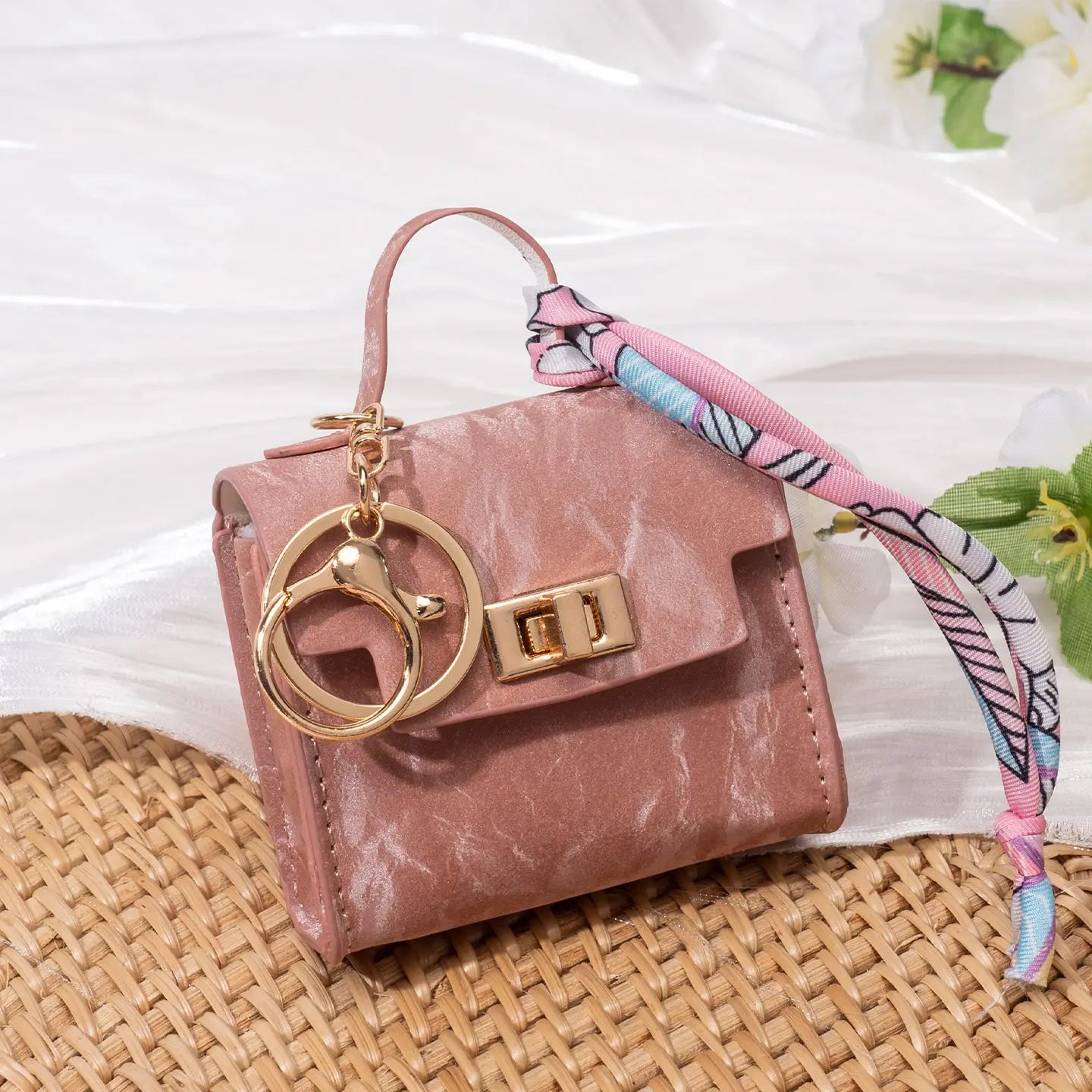 Miniature pink faux leather handbag keychain with gold-tone hardware and patterned ribbon strap featuring a silk scarf detail.
