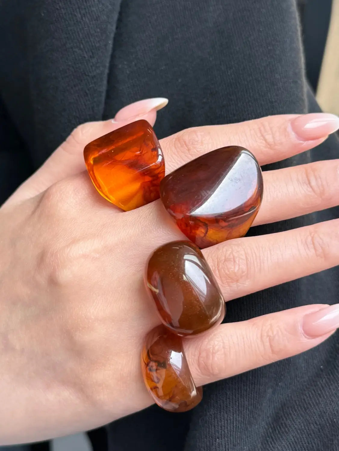 A set of four chunky resin cocktail rings in amber color with polished stone appearance smooth rounded surfaces and natural inclusions.