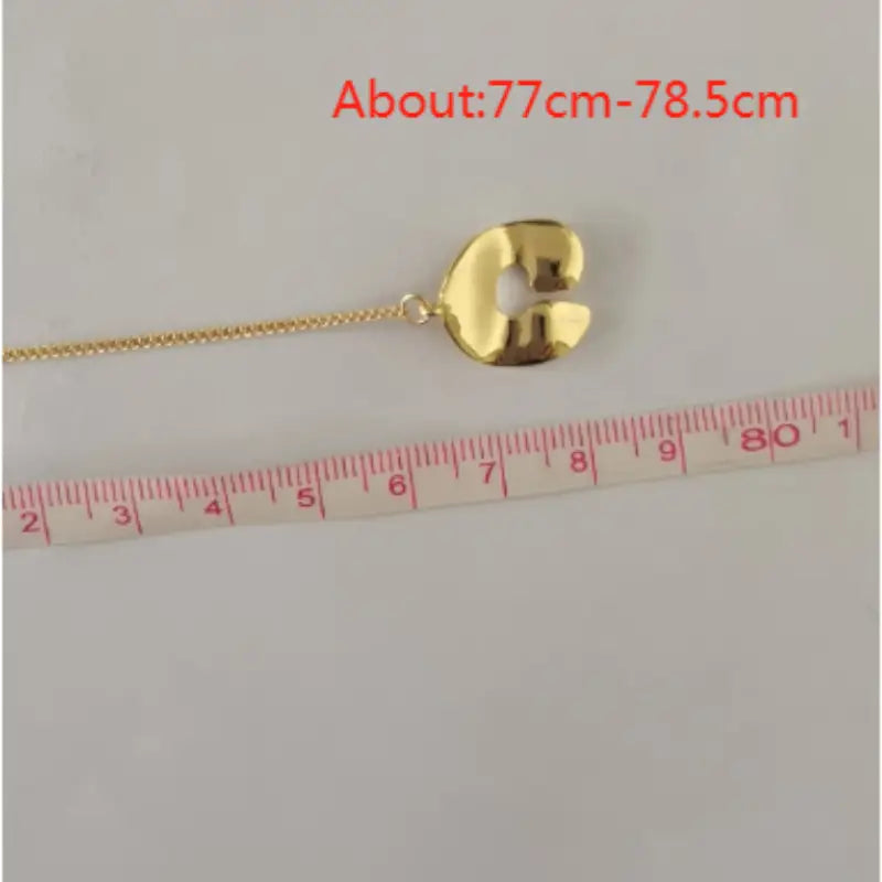 Collier pendentif à superposition géométrique doré pour femmes, présentant un pendentif en métal poli à la couleur dorée, façonné comme une lettre c stylisée, avec une chaînette attachée.
