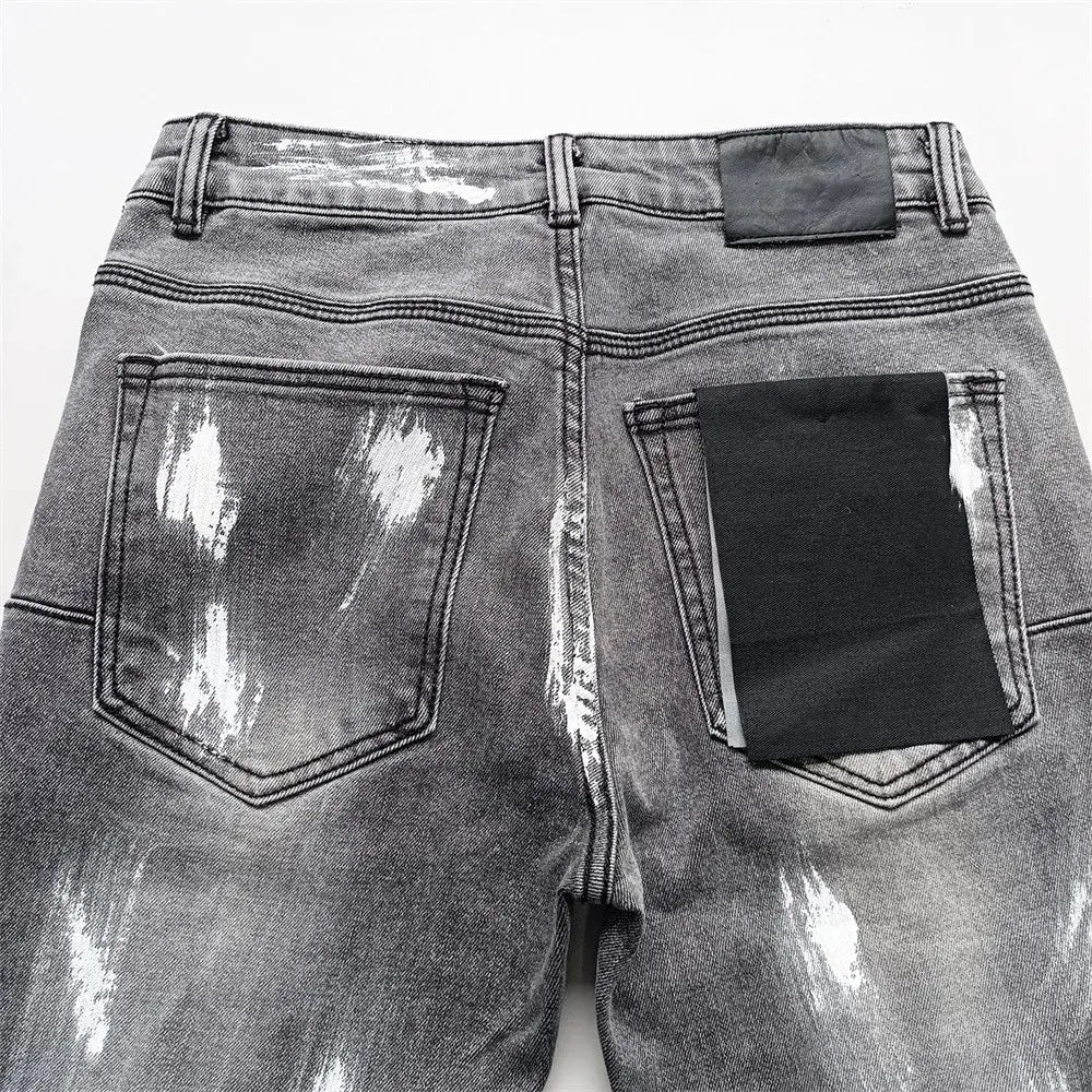 Jeans skinny déchirés pour hommes, effet délavé rétro vintage bleu, présentant le côté arrière du denim gris, avec des effets d’éclaboussures de peinture blanche, et des patchs en tissu noir sur les poches.