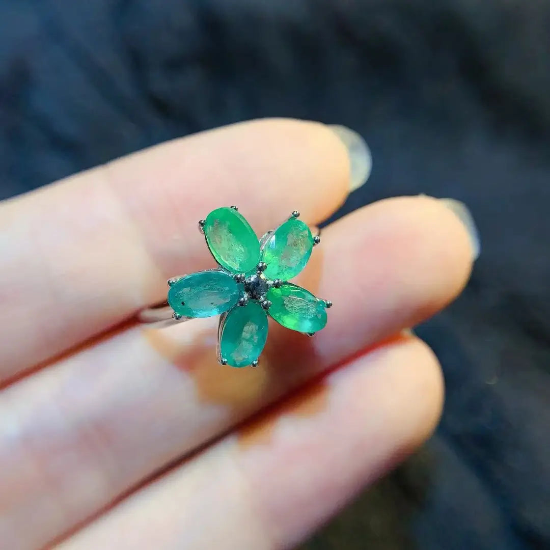 Ein zarter Fünfblüten-Smaragdblumen-Silberring mit lebhaft grünen Edelsteinen, die in einem eleganten silberfarben wirkenden Metall gesetzt sind.