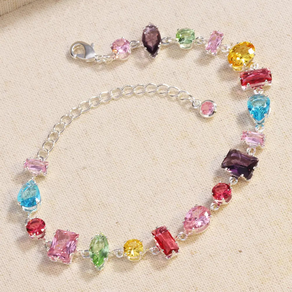 A vibrant multi-colored zircon crystal bracelet with a silver chain featuring faceted stones in pink blue green yellow red and purple.