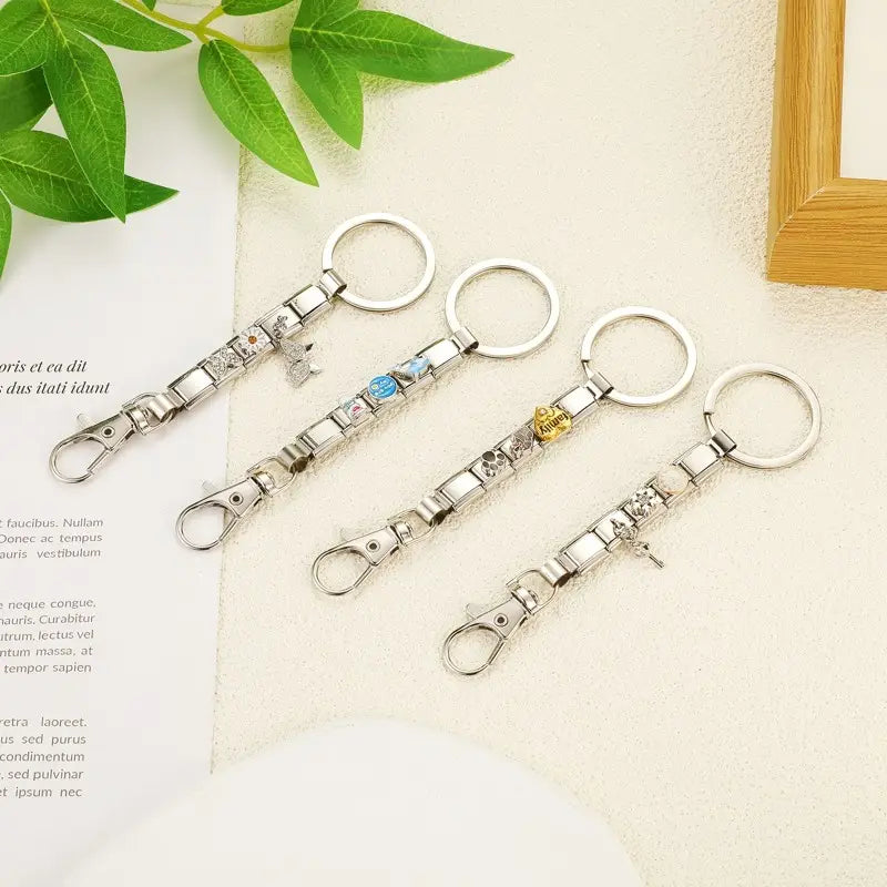 Cuatro llaveros con dije de eslabones italianos con acabado plateado, con broches decorativos que presentan diseños únicos y pequeñas gemas azules, doradas o transparentes para uso personalizado en bricolaje.