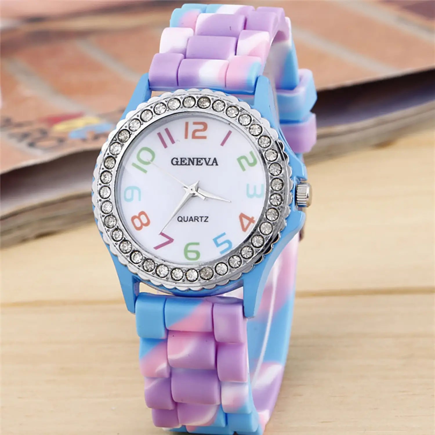 Girls crystal bling rainbow silicone watch featuring a pastel blue and purple silicone band with a white face, rainbow-colored numbers, and a silver bezel adorned with clear rhinestones.