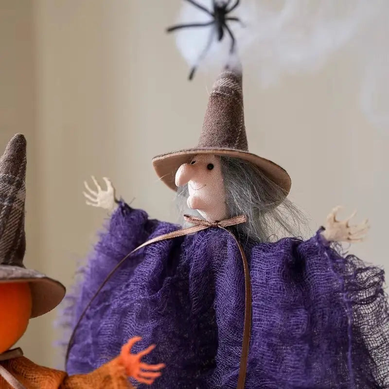 Figura colgante de tela de adorno de halloween de bruja caprichosa con un sombrero marrón de textura, cabello de lana gris y una capa de encaje morado en movimiento.