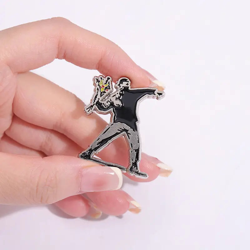 Épingle émaillée noire et argentée présentant une silhouette stylisée en mouvement tenant un objet avec des détails jaunes, inspirée de l’art de rue de Banksy.
