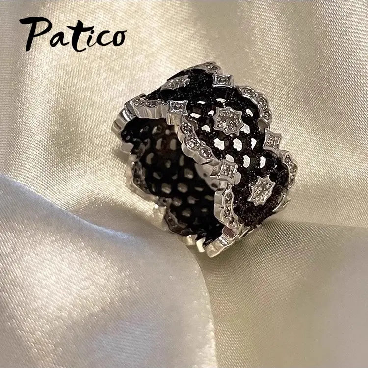 A patico brand sterling silver black geometric ring for women featuring an intricate lace-like design with embedded clear crystals and a silver-toned metal frame.