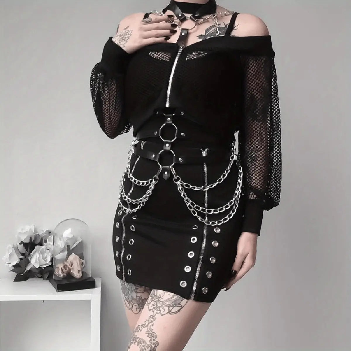 Top de malla negra sin hombros con detalles de cadena y anillos plateados, que incluye una correa corporal con arnés de cuero negro con pentagrama.
