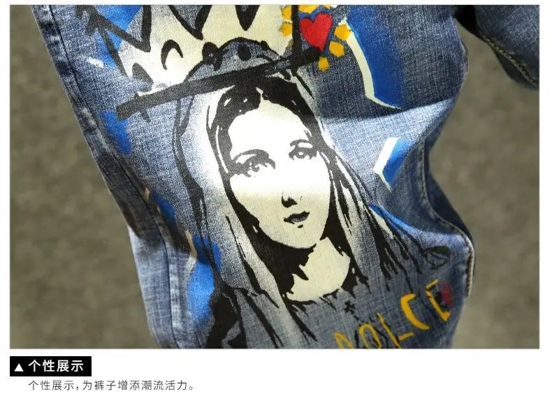 Jean slim imprimé stretch en denim bleu pour homme avec un graphisme stylisé audacieux d’une femme couronnée, présentant des détails noir et blanc rehaussés de cœurs rouges et de lettrage jaune.