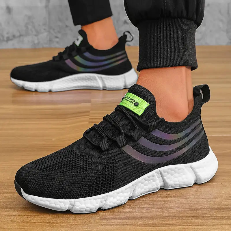 Chaussure de sport noire en maille avec une semelle blanche texturée et des bandes iridescentes, rehaussées d’une étiquette vert néon sur le contrefort, montrant la face arrière des baskets de sport décontractées en maille respirante pour hommes Zuuban.