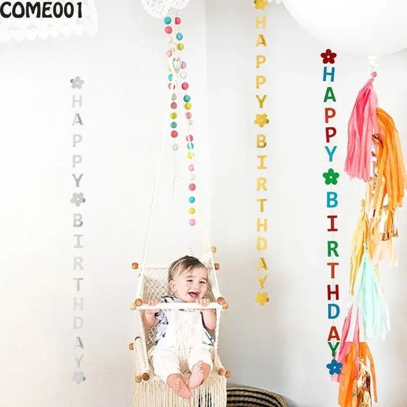 Un bébé joyeux est assis dans une chaise hamac en macramé blanc avec des accents en bois, aux côtés de décorations de guirlandes et de bannières pour un premier anniversaire.