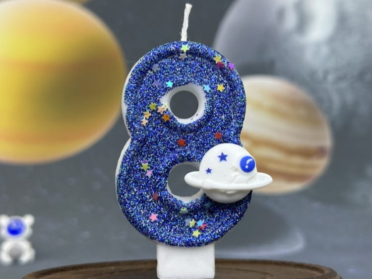 Una vela azul con brillo con el número ocho para cumpleaños, adornada con estrellas de colores y un pequeño dije de nave espacial blanco, para una vela de cumpleaños numeral del espacio, fiesta planetaria, adorno para pastel.