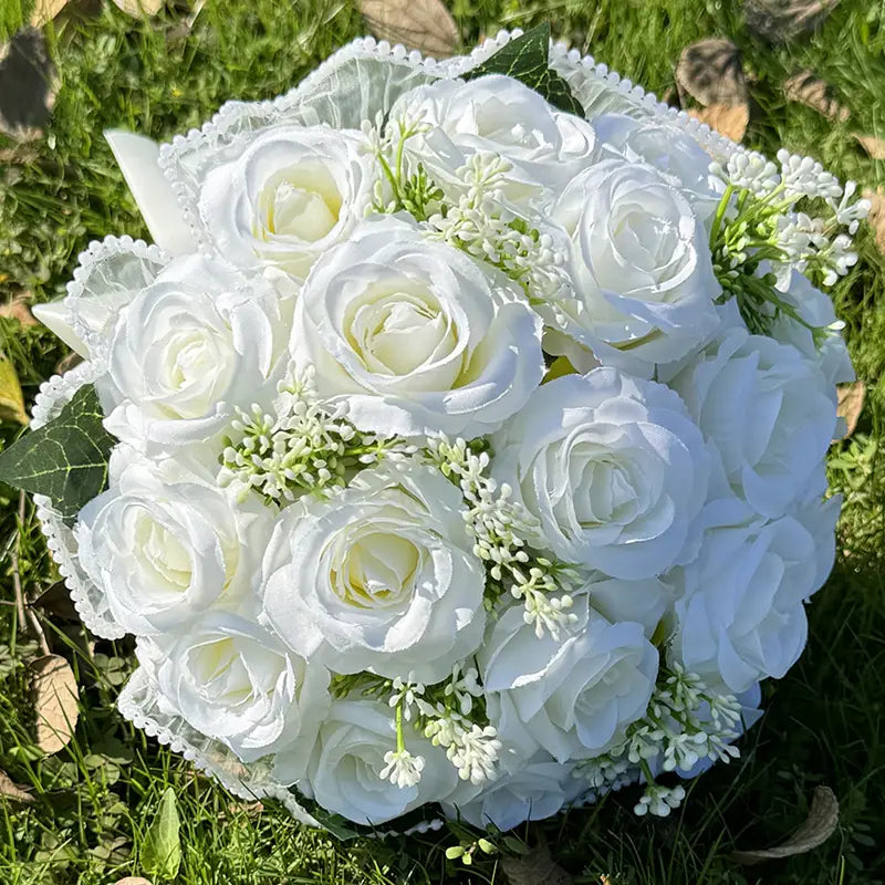 A delicate white silk rose wedding bouquet with lace trim, pearls, and small green filler flowers.